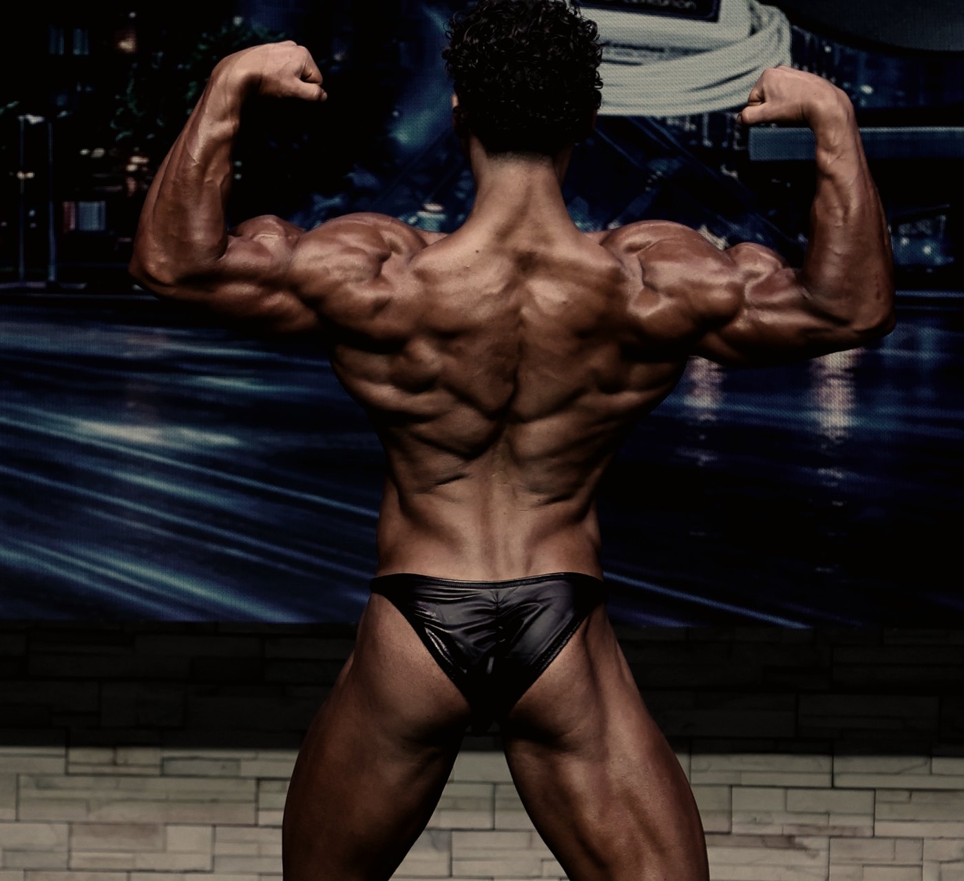 Nicholas Mercanti in a back double biceps pose under low stage lighting